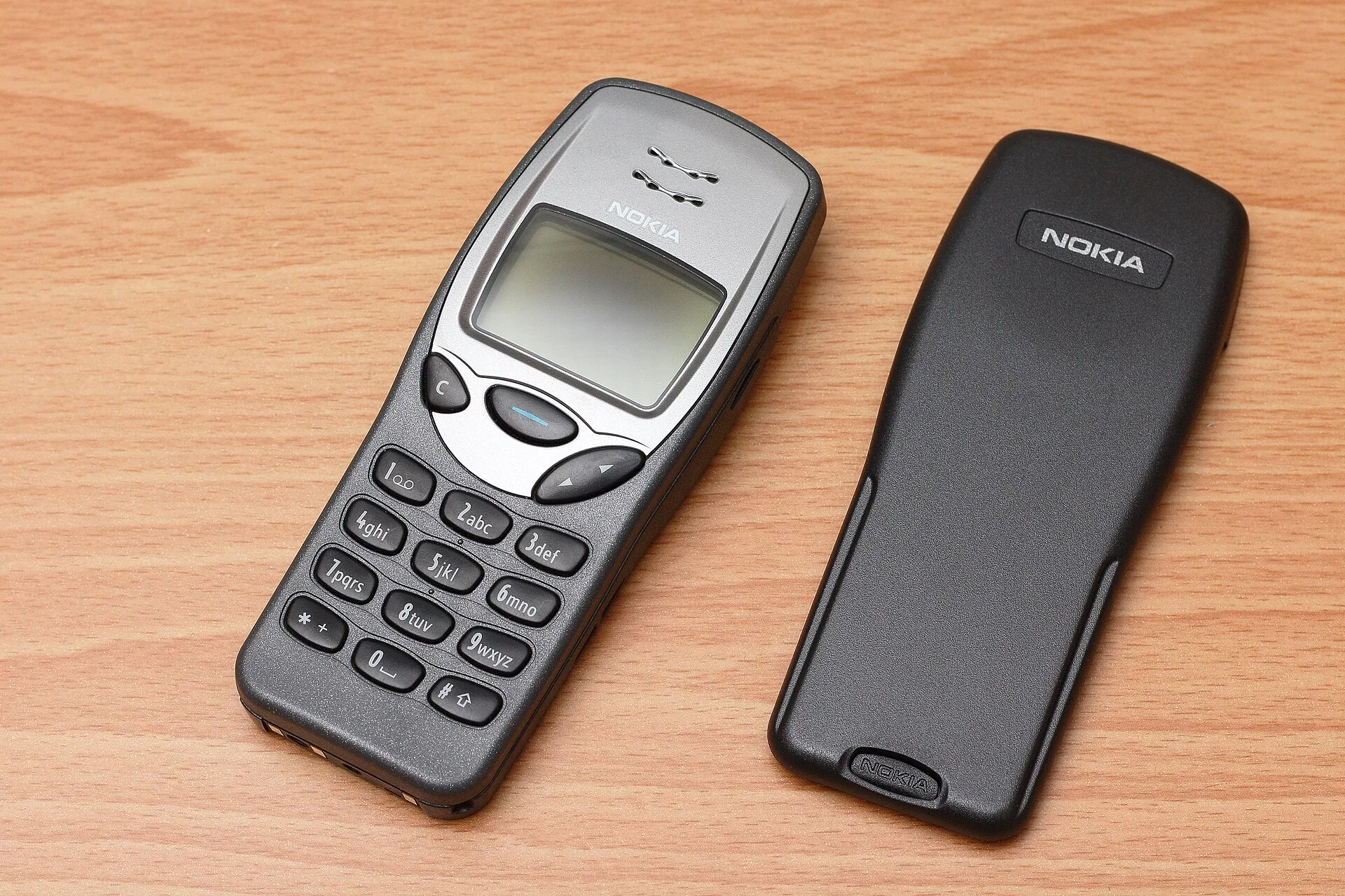 Orijinal Nokia 3210'un önden görünümü ve çıkarılmış arka kapağı ahşap masa üzerinde