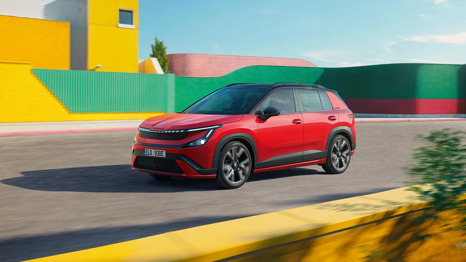 Kırmızı Škoda Epiq Sportline, sarı ve yeşil duvarların önündeki yolda hareket hâlinde